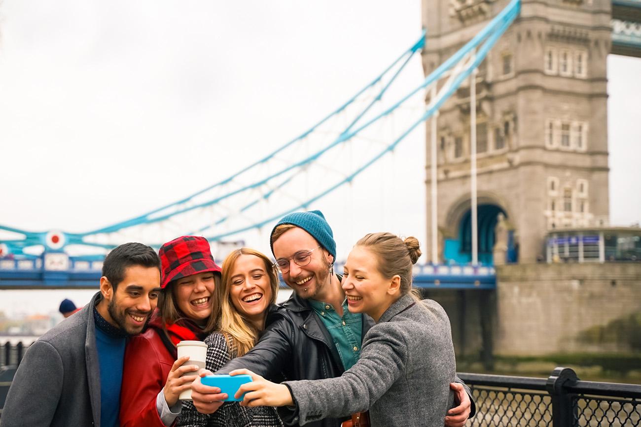 Group of tourists enjoying city tour . Group of friends taking a selfie in London . They are three girls and two boys, embracing and having fun together. 